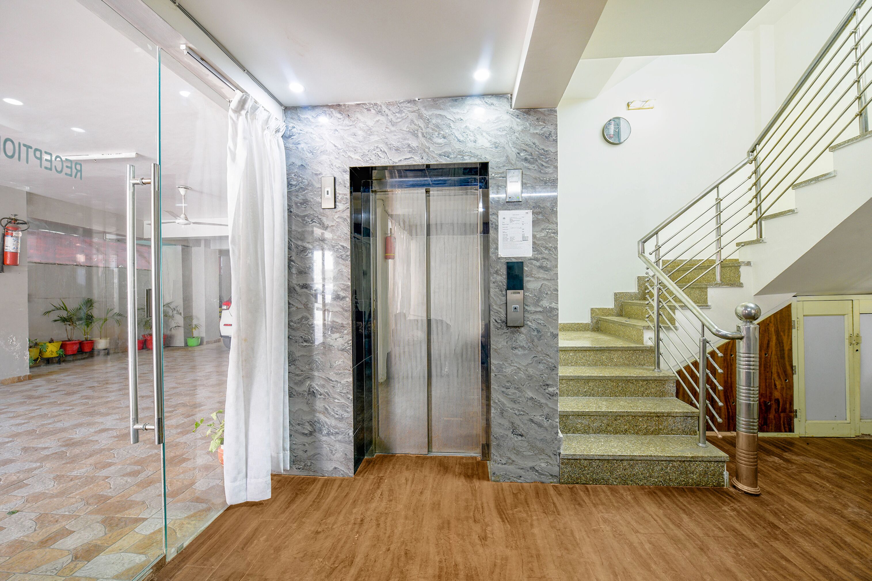 Un ascensor con pared de mármol, suelo de madera y una escalera con barandillas de metal.