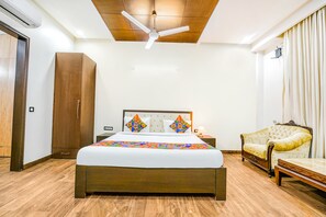 Une chambre à coucher comprenant un lit, une armoire en bois, une table de chevet, une lampe, un canapé et un ventilateur de plafond.