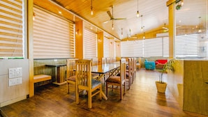 Un amplio comedor con mesas y sillas de madera, un ventilador de techo y ventanas grandes con persianas.