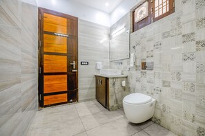 A bathroom with a wooden door, a white sink, a toilet, and patterned tiles. - Fabhotel Prime Happy Feet Luxury Homestay (Dehradun)