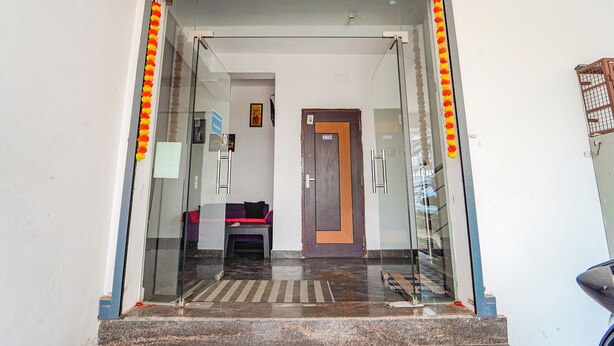 Entrada de hotel con puerta de cristal, una pequeña zona de estar en el interior y una puerta de madera con un letrero en la parte superior.
