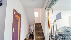 Entrada de hotel con una escalera, un coche estacionado afuera y una puerta con el número 002.