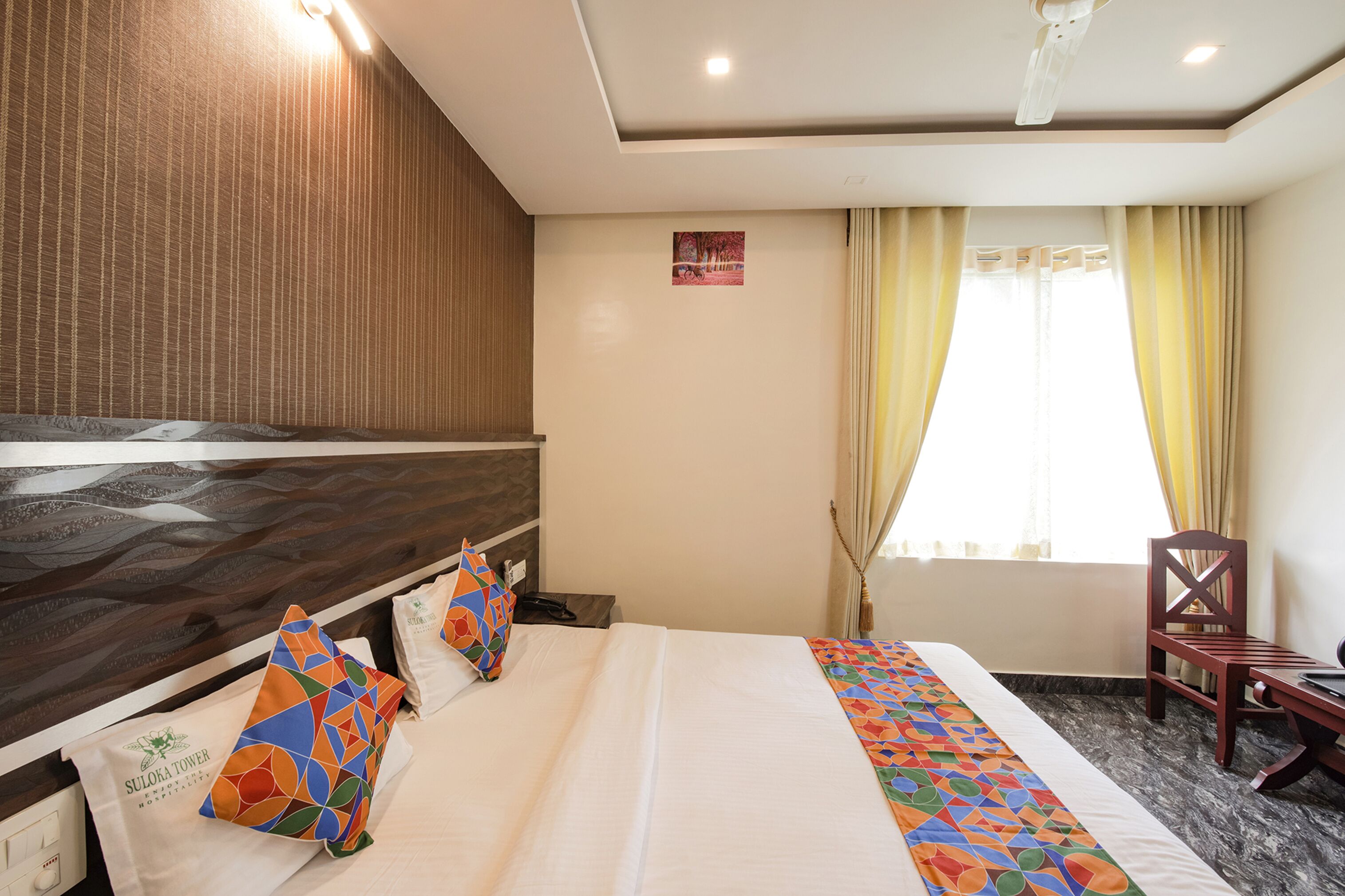 Une chambre d’hôtel avec un lit, une tête de lit en bois, un bureau et une chaise.