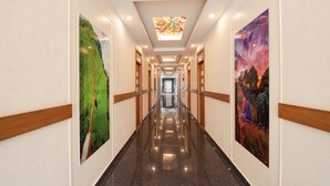 A long, well-lit hallway with wooden paneling and artwork on the walls. - Fabhotel Prime Suloka Towers (Kushalnagar)