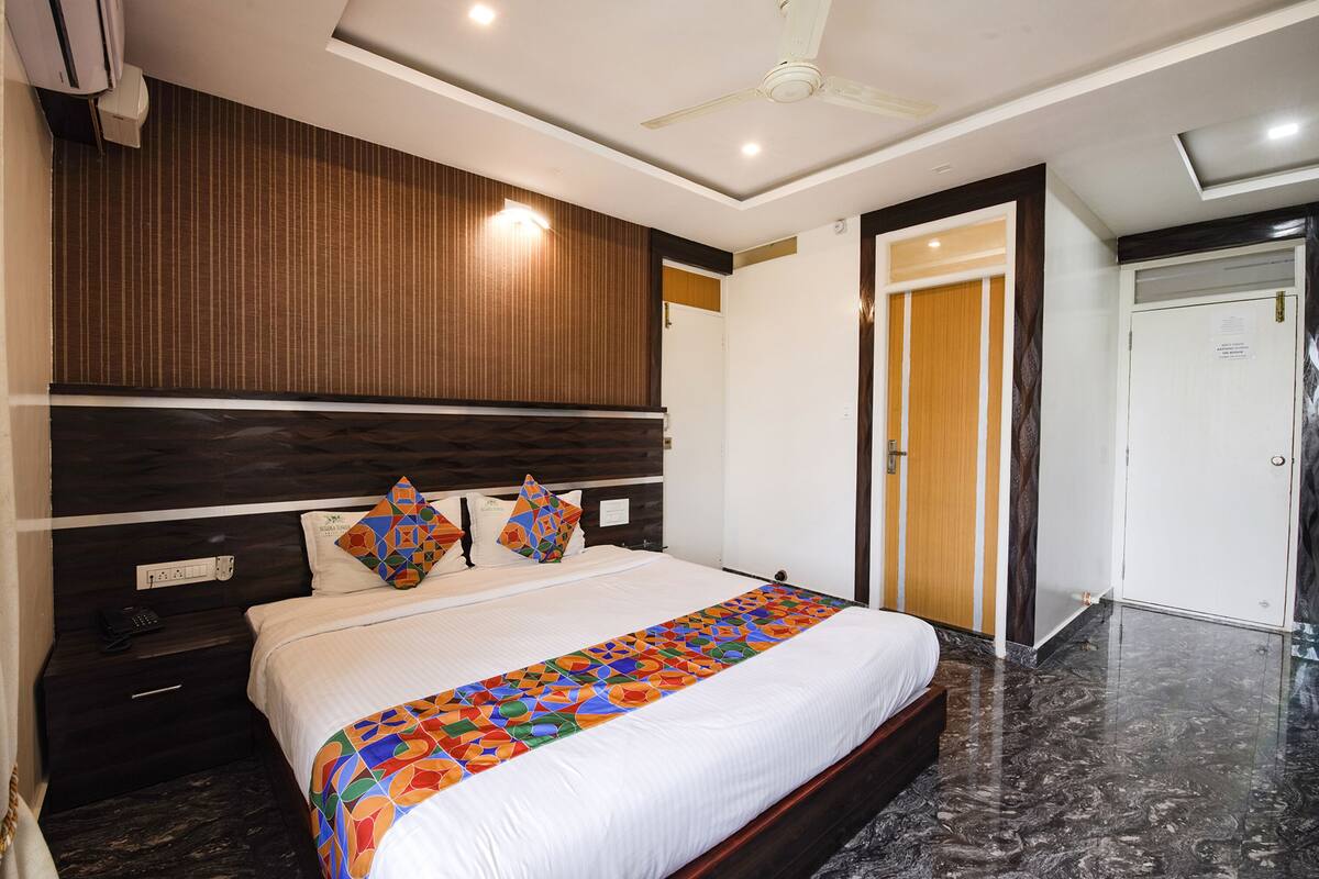 A hotel room with a large bed, a wooden headboard, a nightstand with a phone, and a door leading to another room.