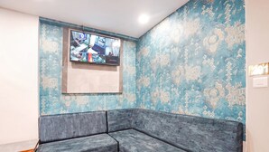 Ein Eckzimmer mit grauem Ecksofa, einem an der Wand befestigten Fernseher und Wandpapier mit Muster.