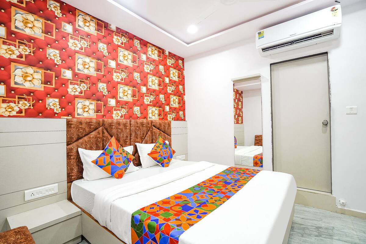 A hotel room with a large bed, a red patterned wall, a brown headboard, and a white bedside table.