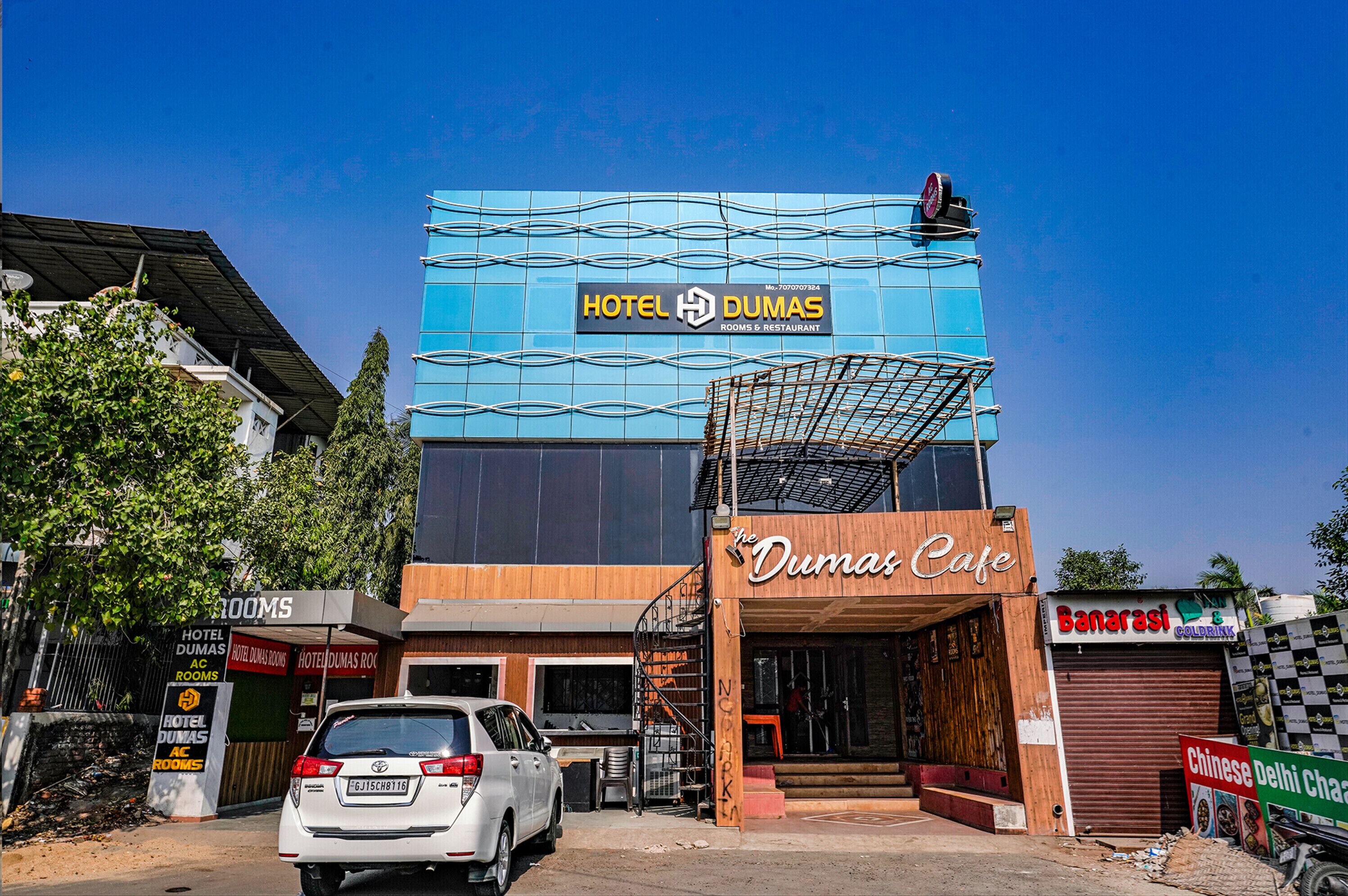 Un hotel con fachada azul, una cafetería y un cartel que anuncia 'Banaras Gold Drink'.