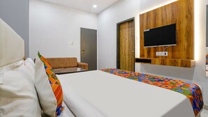 Una habitación de hotel moderna con cama, sofá, televisor montado en un panel de madera y una puerta.