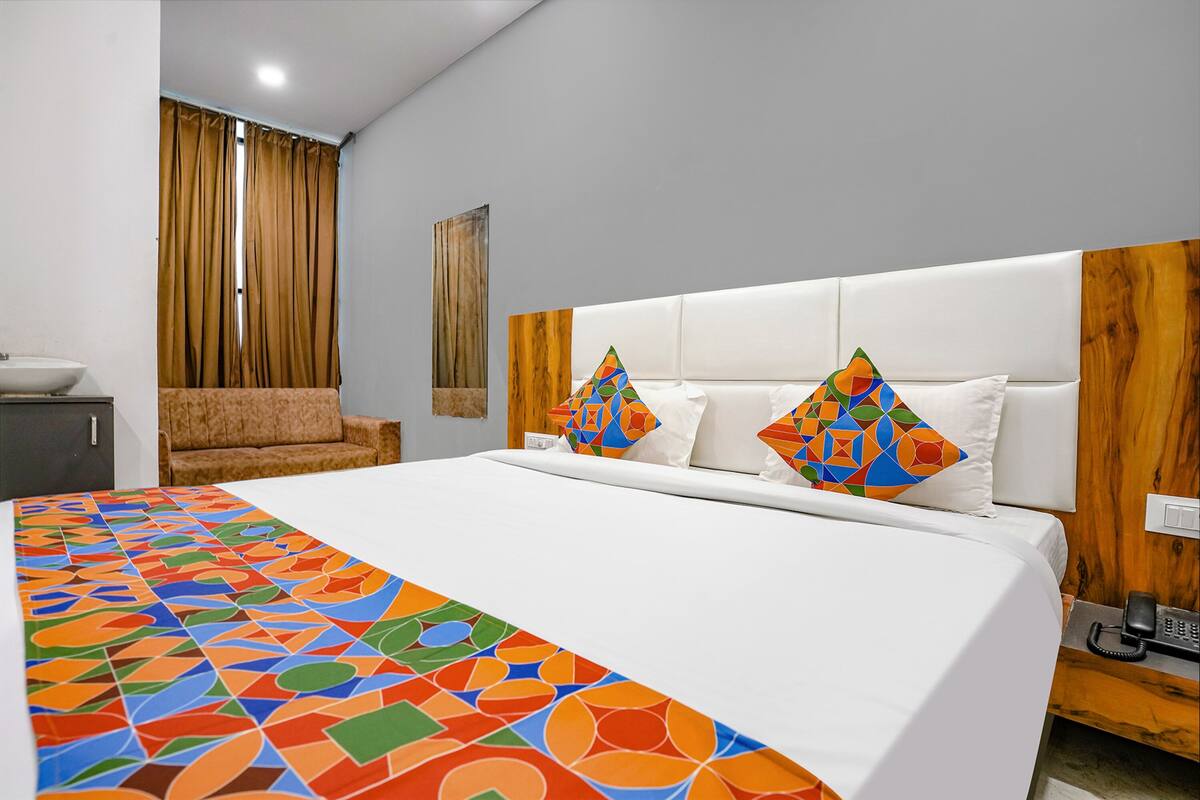 A hotel room with a large bed, a sofa, a wooden headboard, and a telephone on a wooden side table.
