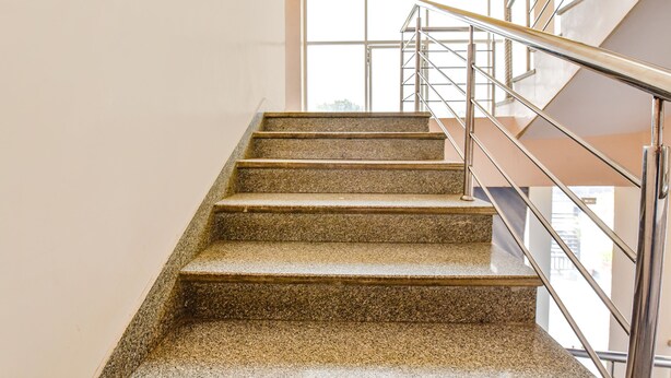 Un escalier avec des marches en granit et des rampes en métal, menant à l’étage supérieur.