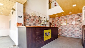 Un comptoir d’accueil avec une enseigne indiquant « fab hotels », des carreaux muraux à motifs et un ventilateur de plafond.