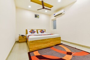 A bedroom with a wooden bed, a ceiling fan, an air conditioning unit, a nightstand, and a patterned rug. - Fabhotel Bhanwar Niwas (Jaipur)