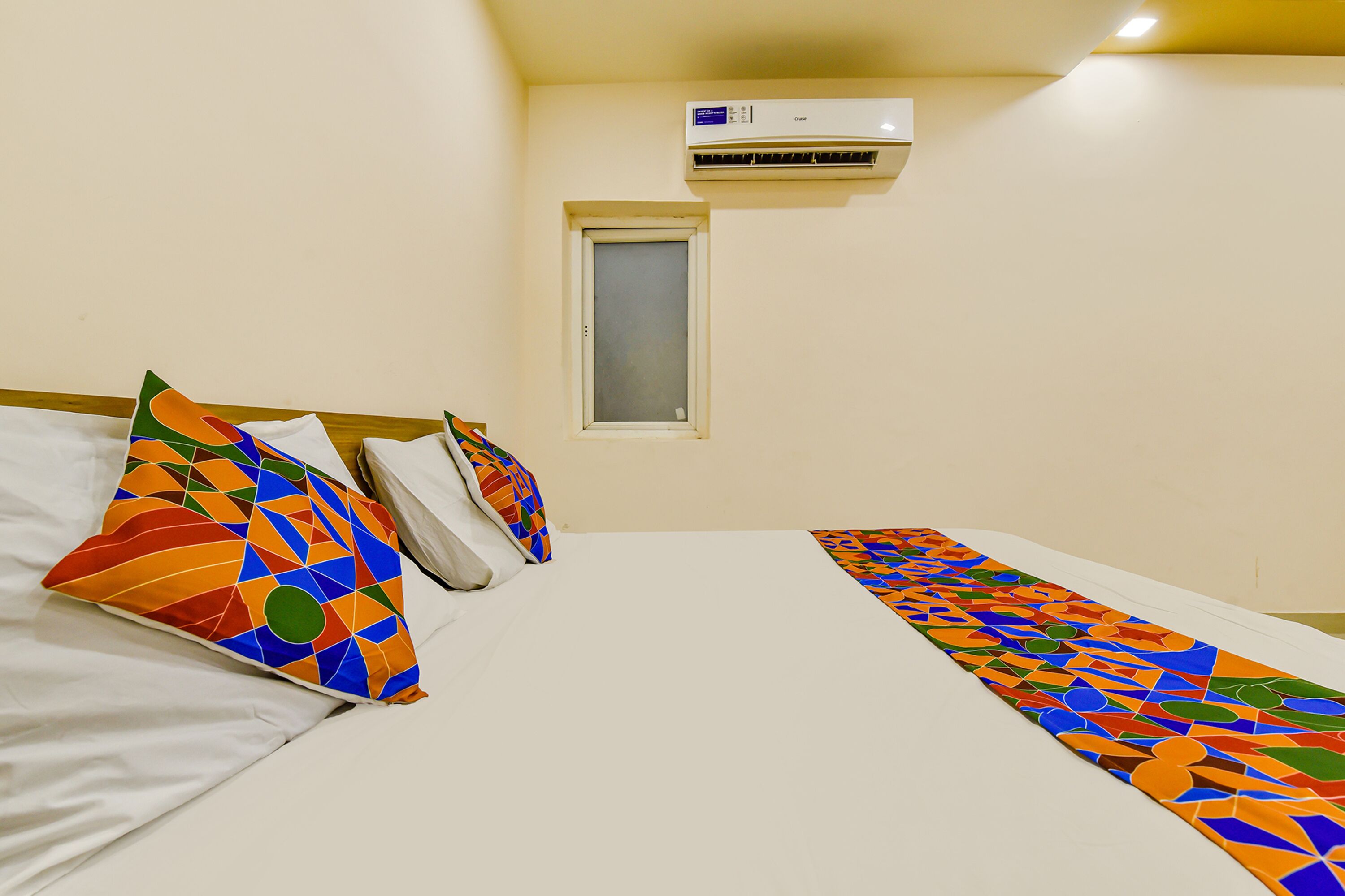 Una habitación de hotel con cama, almohadas, ventana y aire acondicionado.