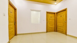 Une pièce avec trois portes en bois, un sol carrelé et une petite fenêtre.