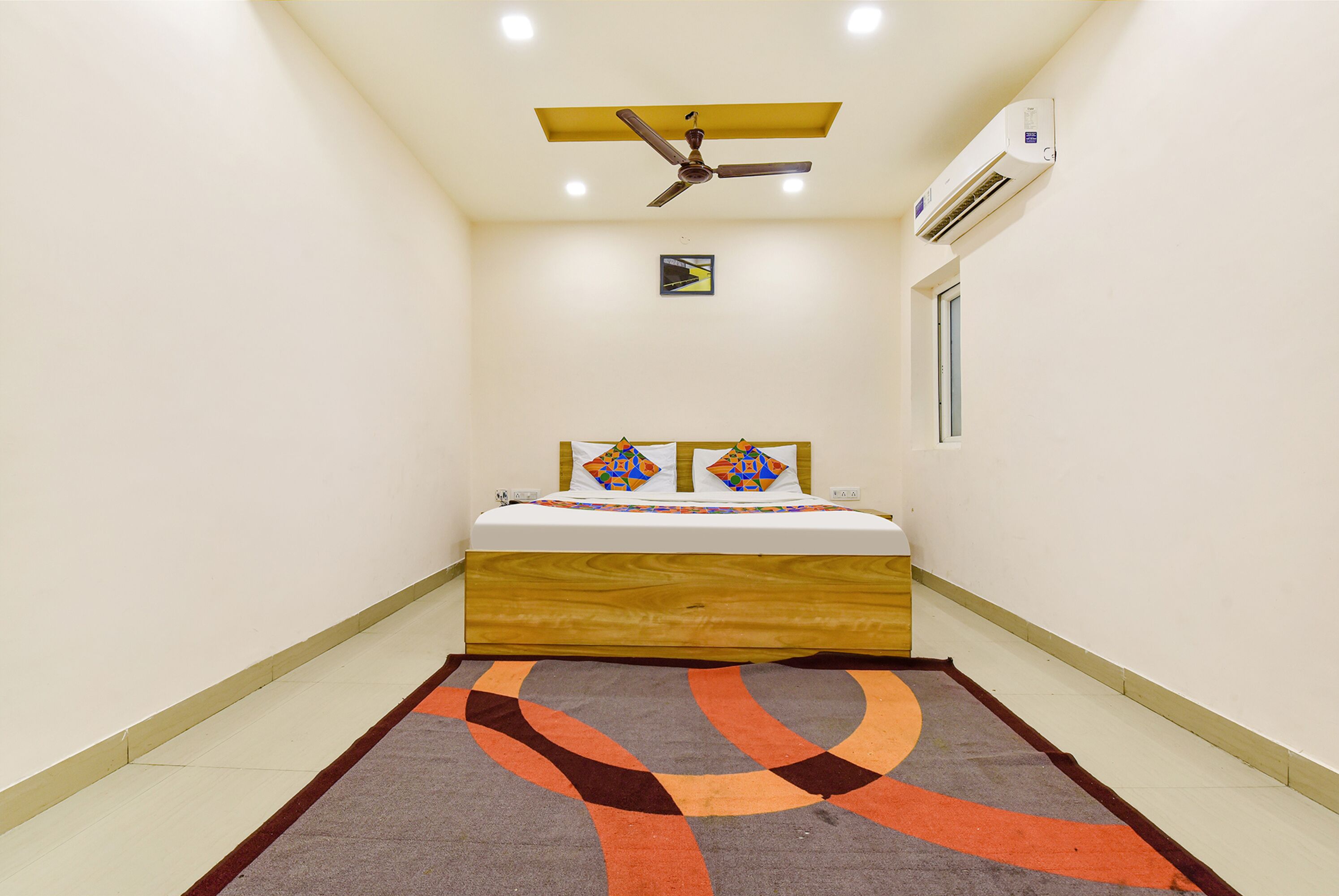 Une petite pièce comprenant un lit, un ventilateur de plafond, un appareil de climatisation et un tapis à motifs.