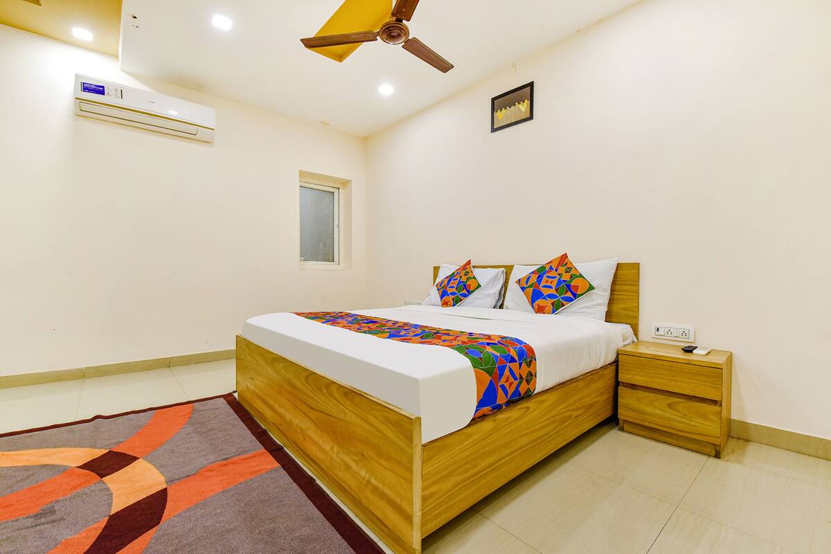 A bedroom with a wooden bed, a nightstand, a ceiling fan, an air conditioner, and a window.