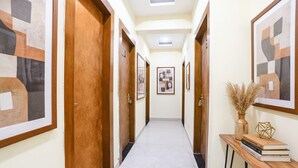 A hallway with wooden doors, framed artwork, and a small table with books and a vase. - Fabexpress Aditya Guest House (Varanasi)