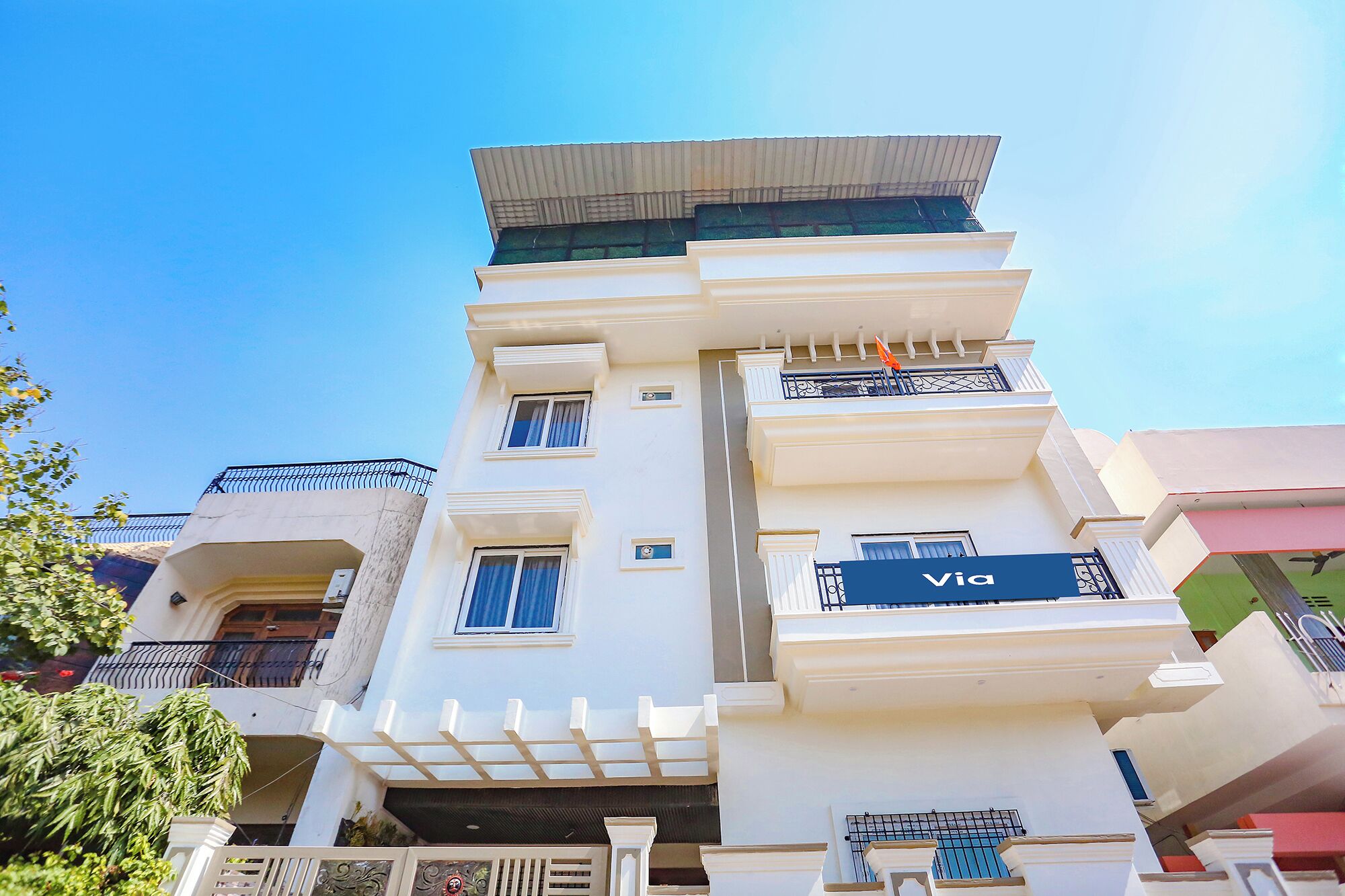 A multi-story building with balconies, a sign reading 'Via,' and a clear blue sky.