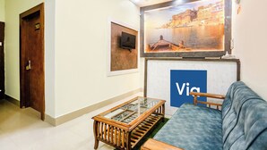 A room with a sofa, a glass-top coffee table, a TV, a door with a number, and a large framed picture on the wall. - Fabexpress Aditya Guest House (Varanasi)