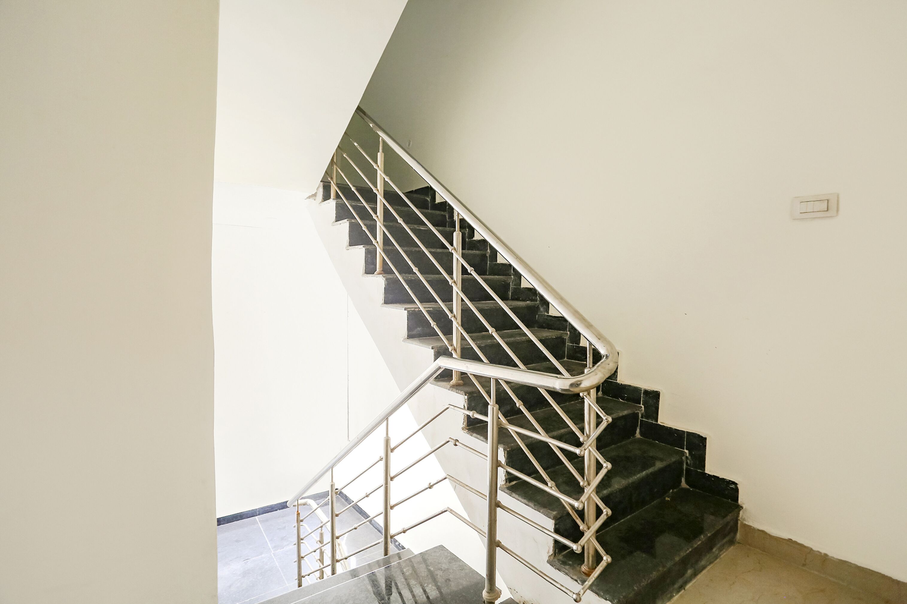 A staircase with a metal railing, a light switch on the wall, and a tiled floor.