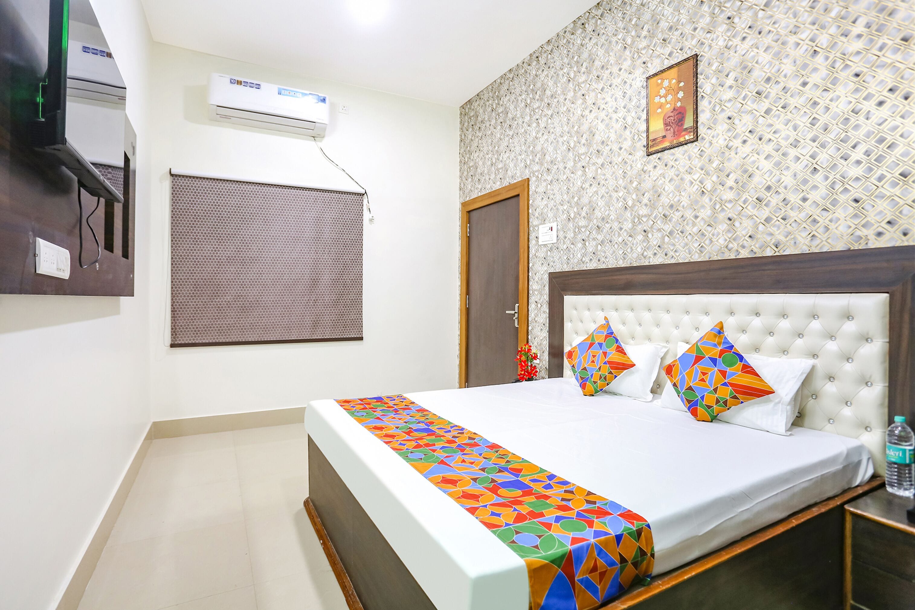 A hotel room with a bed, air conditioning unit, window with blinds, and a decorative wall.