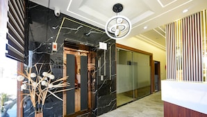 Un área de recepción moderna con un mostrador de mármol, un jarrón de madera con plantas secas e iluminación empotrada en el techo, además de una lámpara circular.