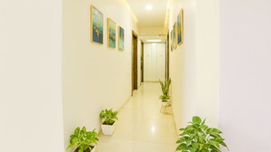 A hallway with white walls, several framed artworks, and potted plants. - FabHotel Kuber (Navi Mumbai)
