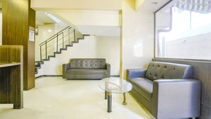 A lobby with a staircase, two sofas, a glass table, and a wooden column. - FabHotel Kuber (Navi Mumbai)