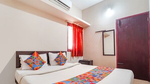 Quarto de hotel com cama, mesa de cabeceira, janela com cortinas vermelhas e porta.