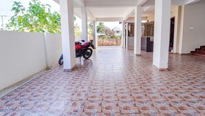 Uma área externa coberta com piso de azulejos, uma motocicleta estacionada à esquerda e uma escadaria que leva a um nível superior.