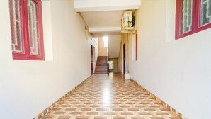 Um corredor com chão de madeira estampada, paredes brancas e janelas com moldura vermelha.
