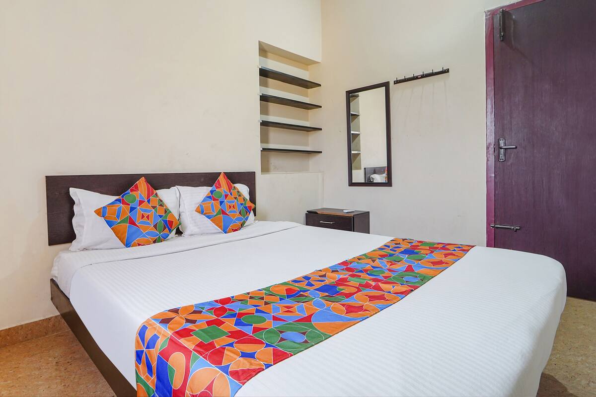 A neatly made bed with a colorful geometric-patterned bed runner, a white pillow, and a matching pillow on a dark headboard.