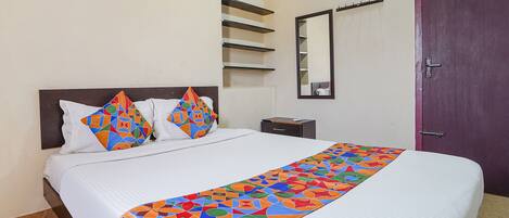 Una cama bien tendida con un corredor de cama de estampado geométrico colorido, un almohadón blanco y otro a juego en un cabecero oscuro.