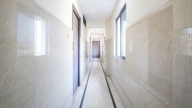 A corridor with marble walls and a tiled floor, leading to a door at the end. - Fabhotel Sai National (Visakhapatnam)
