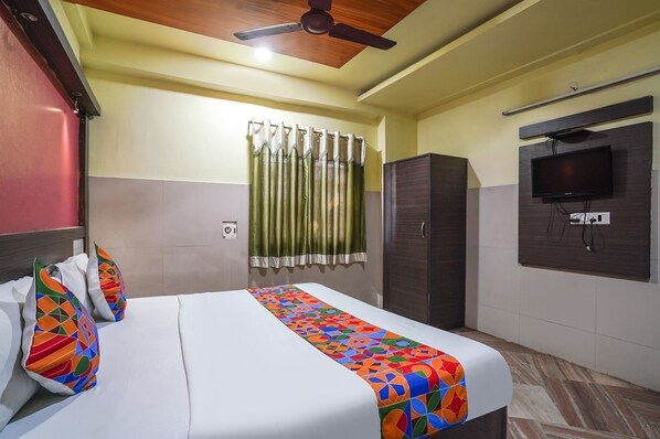 A hotel room with a bed, a wardrobe, a television mounted on the wall, and a ceiling fan.