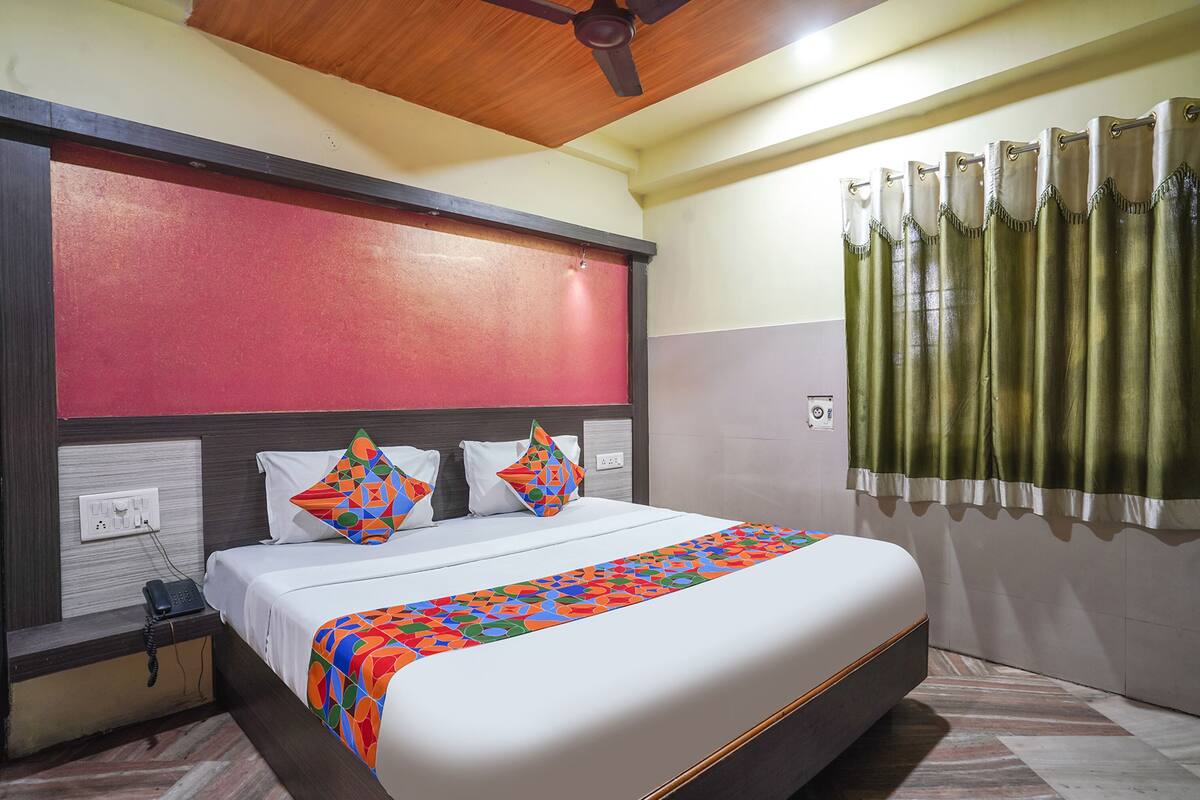 Habitación de hotel con una cama grande, ventilador de techo de madera, teléfono en la mesita de noche y cortina con un frente verde.