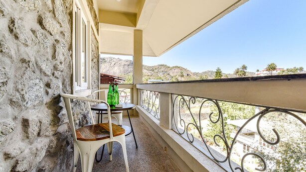 En balkon med en stenvæg, et bord med en stol og udsigt over et bjergrigt landskab.
