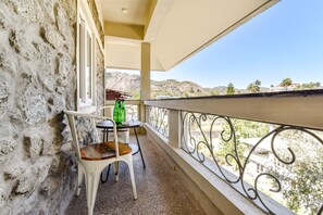 Un balcón con un muro de piedra, una mesa con una silla y vistas a un paisaje montañoso.