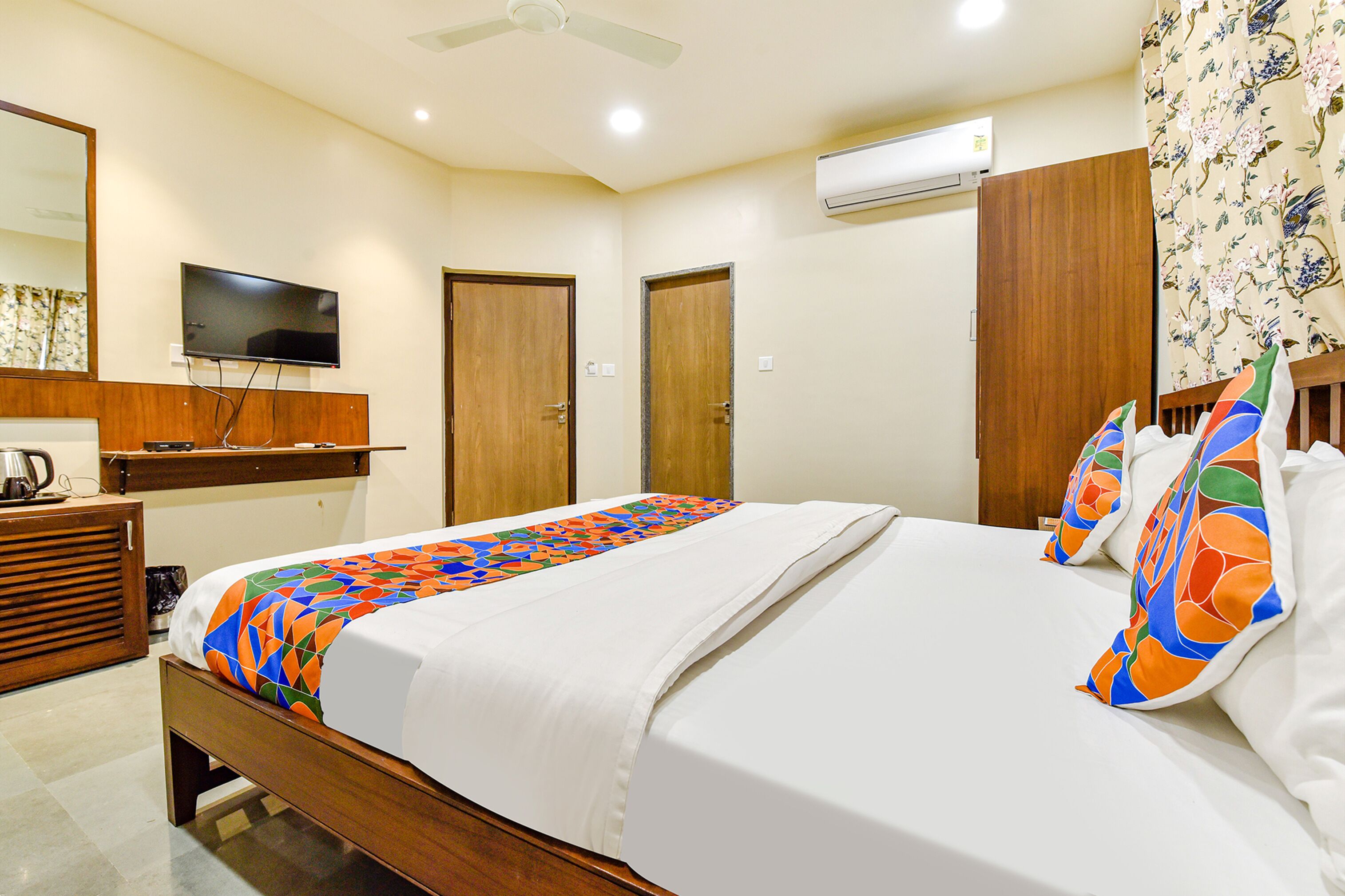 A hotel room with a bed, a television, a wooden desk, and a wardrobe.