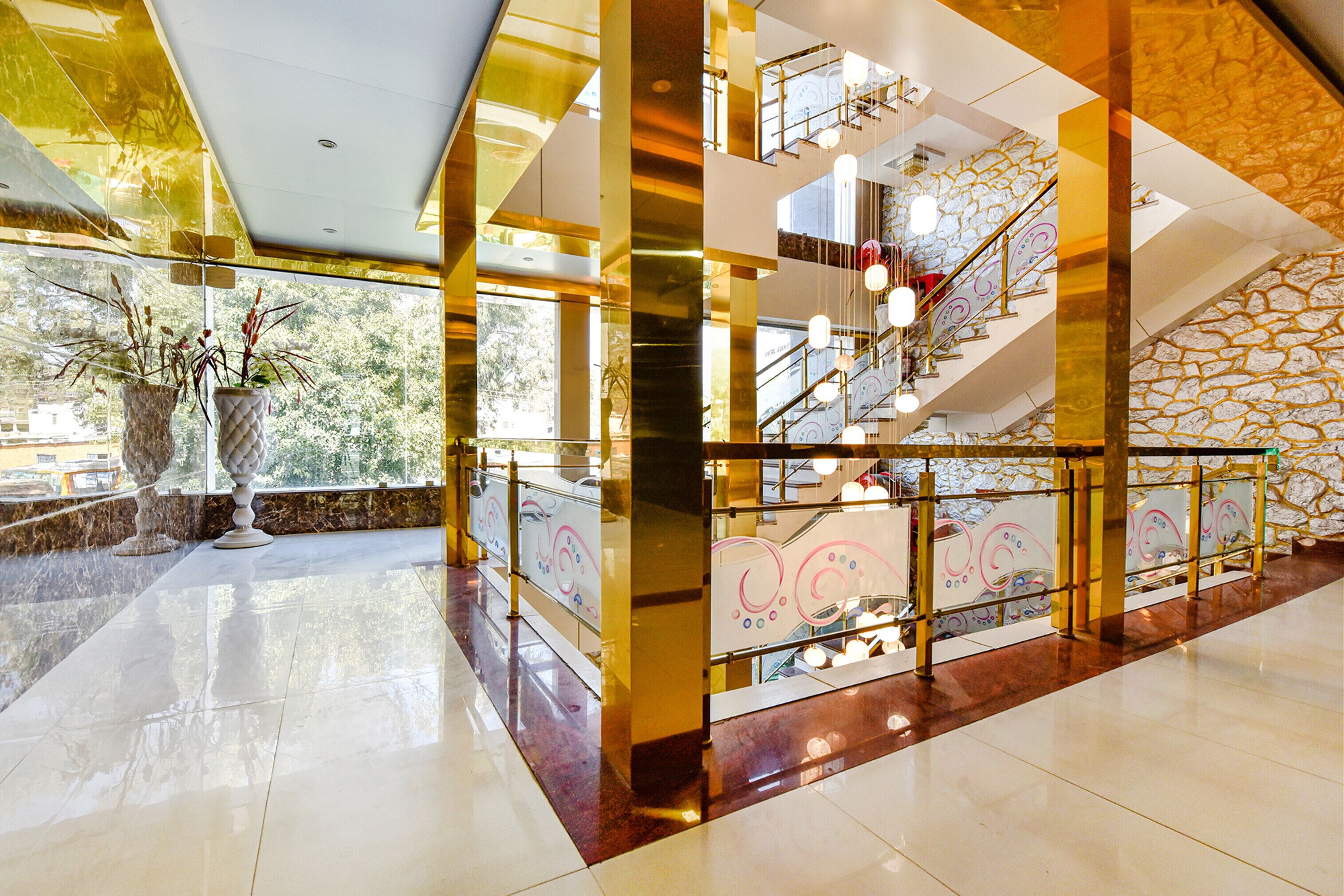 A spacious lobby with a marble floor, a staircase with glass railings, and decorative plants.