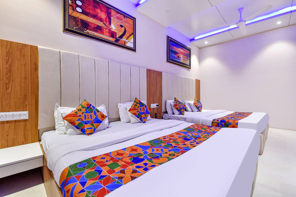 Habitación de hotel con dos camas, cabecero de madera y manta geométrica de colores.