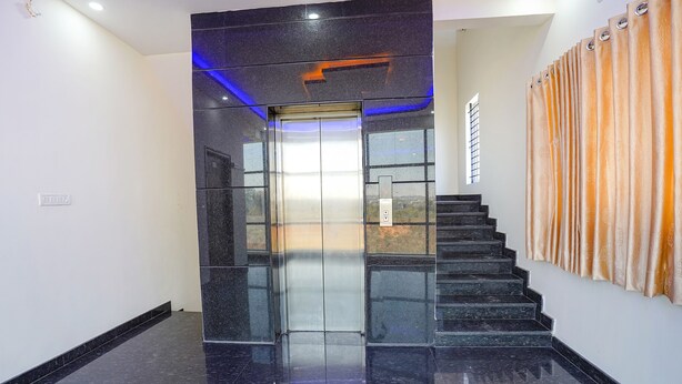 A modern elevator with a glass door, a staircase with black steps, and a wall with patterned curtains. - Fabhotel Sri Ram Comforts (Bengaluru)