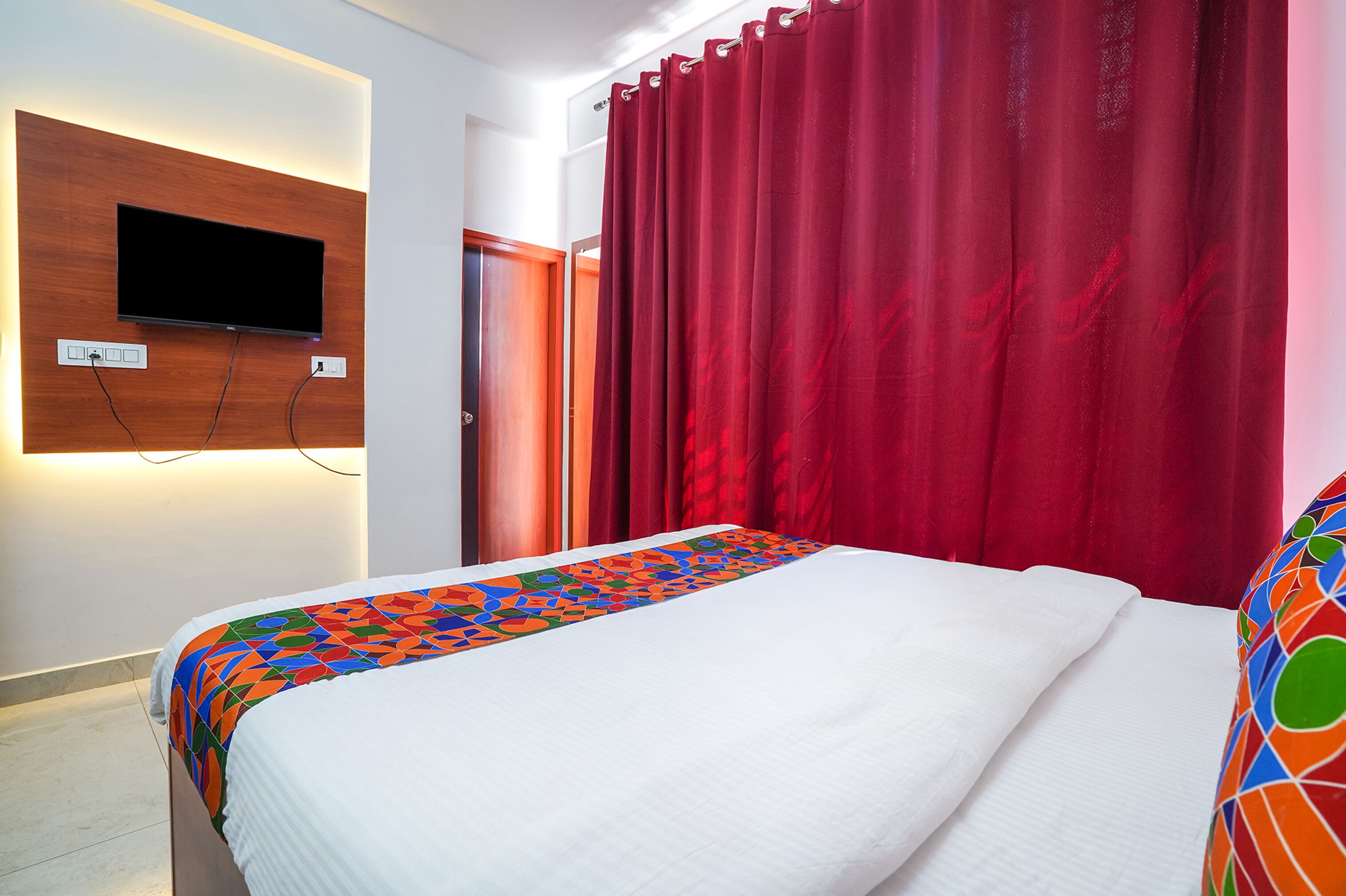 Una habitación de hotel con cama, televisor montado en la pared y cortinas rojas.