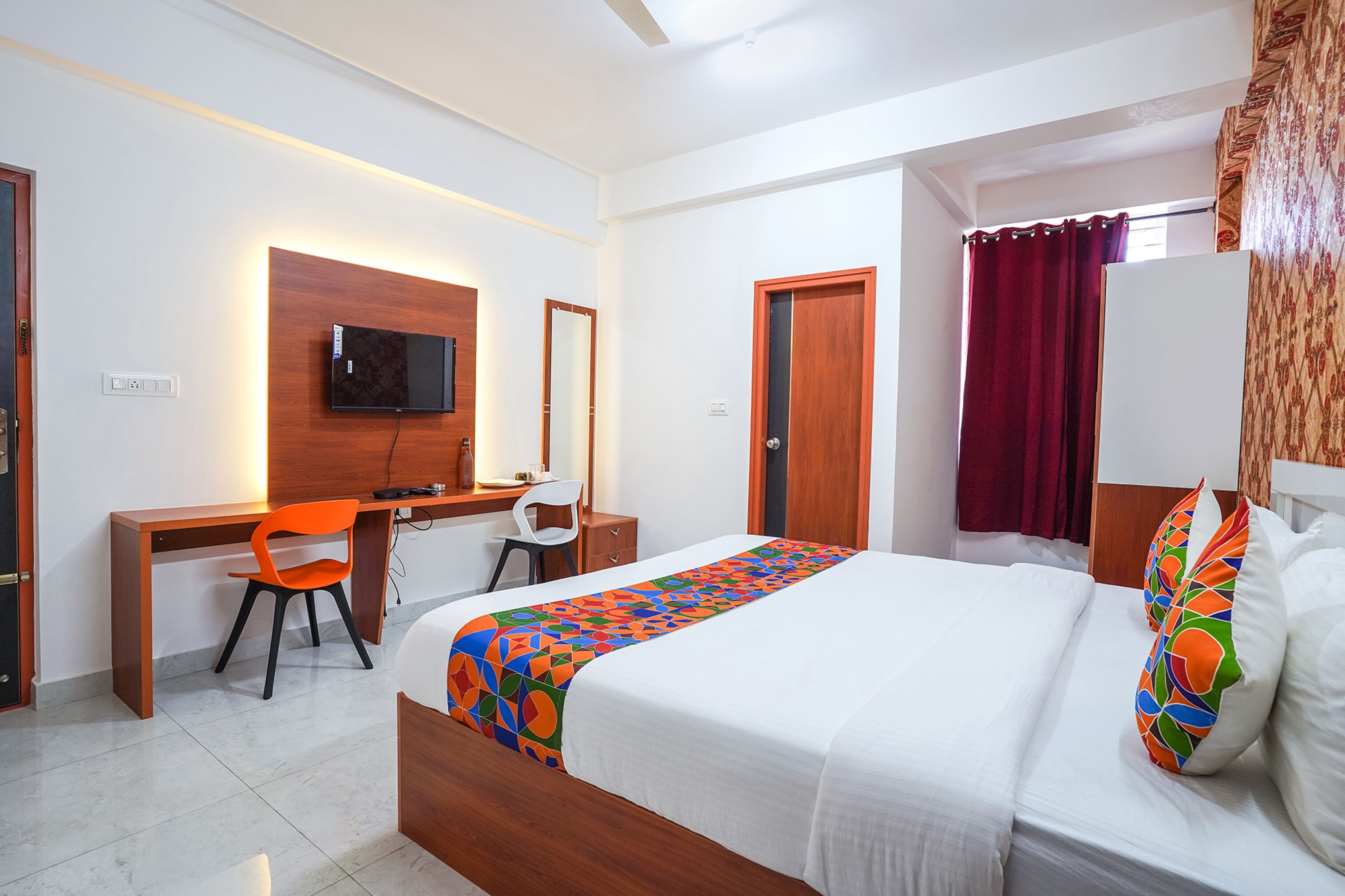 Une chambre d’hôtel comprenant un lit, un bureau avec une chaise, un téléviseur fixé au mur et une fenêtre avec des rideaux.