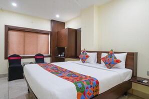A hotel room with a large bed, two chairs, a wardrobe, and a window with blinds. - Fabhotel Gvr Grand (Vijayawada)