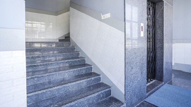 Un escalier aux marches et aux murs en marbre, menant à une porte ornée d’une grille métallique.