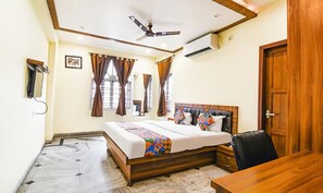 A bedroom with a bed, a ceiling fan, an air conditioning unit, a wooden desk, and a door.
