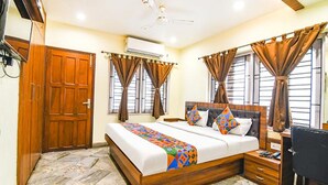 A bedroom with a wooden bed, a desk, and a chair. There is a wardrobe and an air conditioning unit on the wall. - Fabexpress Duplex Villa (Barasat)