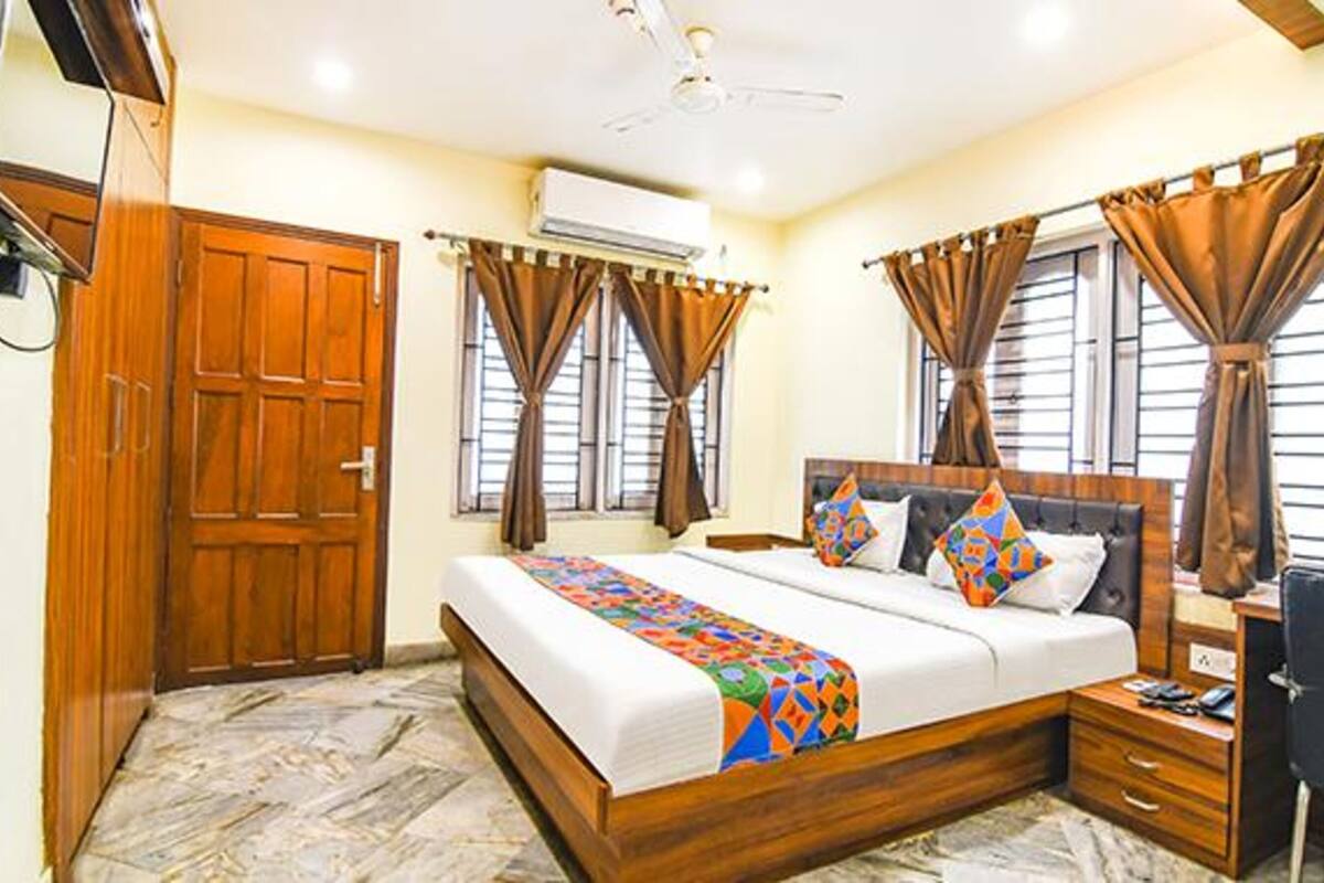 A bedroom with a wooden bed, a desk, and a chair. There is a wardrobe and an air conditioning unit on the wall.